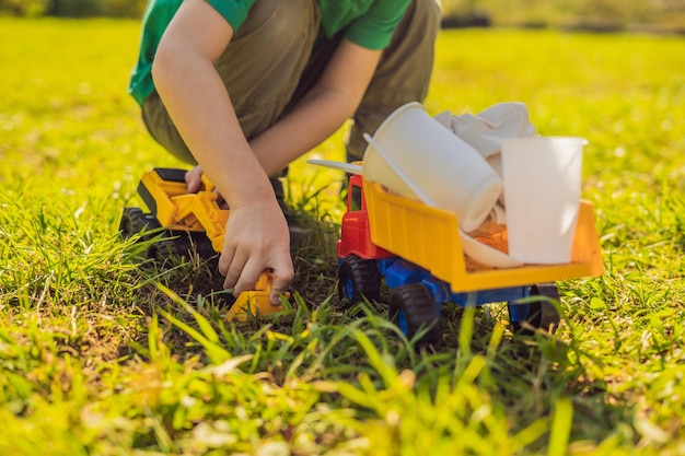 Zdjęcie chłopiec bawi się w recykling zakopuje plastikowe naczynia jednorazowe i naczynia biodegradowalne