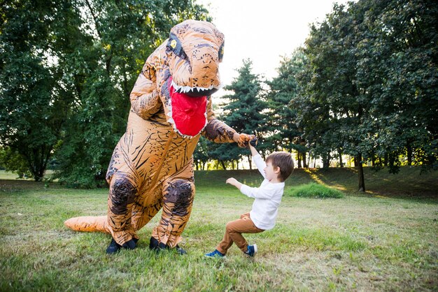 Zdjęcie chłopiec bawi się z osobą w kostiumie dinozaura w parku