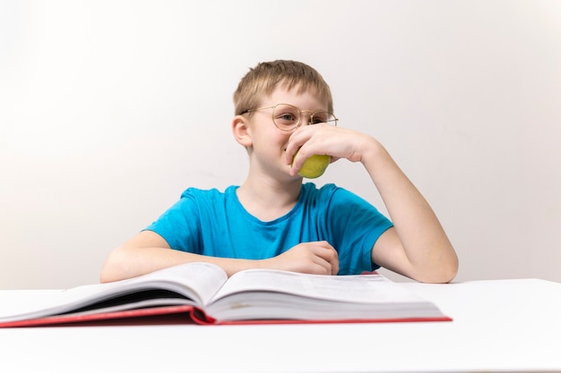 Chłopiec czyta książkę i je książkę uczeń w okularach odrabia pracę domową zamyślony uczeń czyta