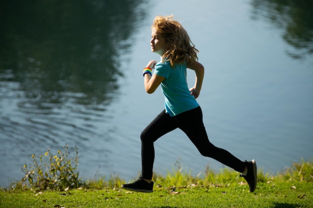 Chłopiec dziecko bieganie lub jogging w pobliżu jeziora na trawie w parku sportowy chłopiec biegacz biegający w akcie parku lato