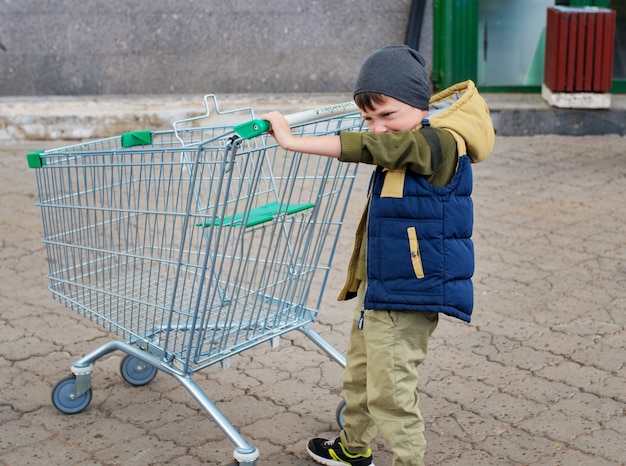 Chłopiec dziecko pcha pusty wózek na zakupy na parkingu