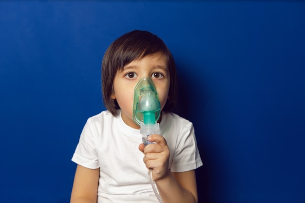 Chłopiec Dziecko Poddawane Leczeniu Oddycha Zieloną Maską Inhalacyjną Na ścianie Niebieskiej ściany W Klinice Dziecięcej