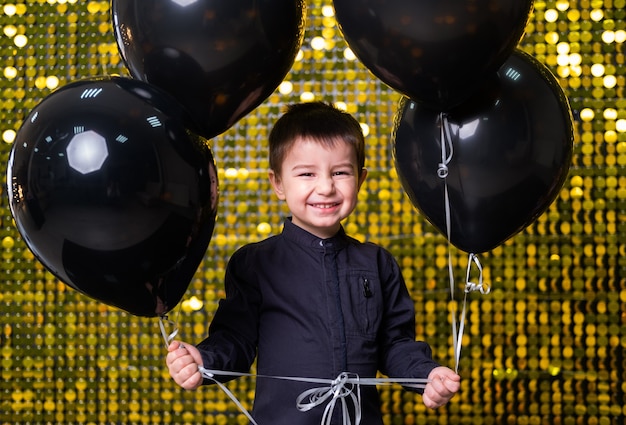 Chłopiec dziecko trzyma czarne balony nad złotymi błyszczącymi cekinami paillettes