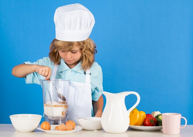 Chłopiec dziecko w kapeluszu szefa kuchni i fartuchu, gotowanie, przygotowywanie posiłku, mały kucharz z warzywami w kuchni naturalnej