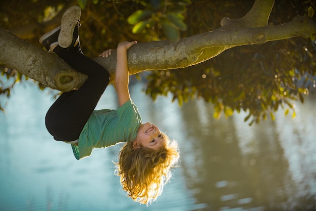 Zdjęcie chłopiec dziecko wspinające się na wysokie drzewo w letnim parku portret słodkiego chłopca siedzącego na drzewie wspinającego się na drzewo aktywny chłopiec bawiący się w ogrodzie koncepcja stylu życia dzieci dzieci na wsi