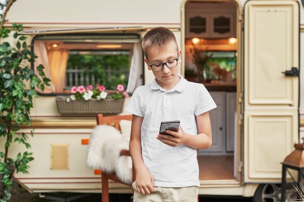 chłopiec dziecko z telefonem na wakacjach w lecie w pobliżu domu na kółkach