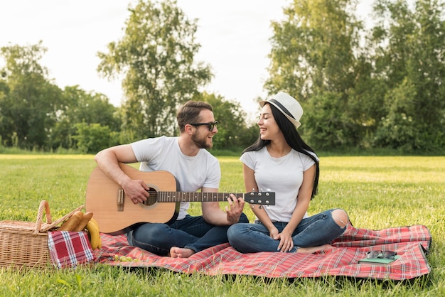 Chłopiec gra na gitarze dla swojej dziewczyny na koc piknikowy