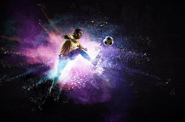 Chłopiec grający w piłkę nożną uderzając piłkę na kolorowym tle. Różne środki przekazu