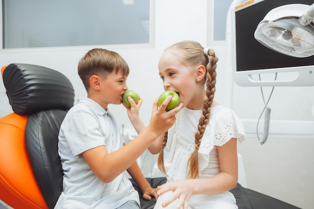 Chłopiec i dziewczynka jedzą jabłka na fotelu dentystycznym koncepcja zdrowych zębów dzieci jedzą zielone jabłko