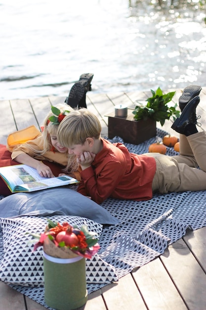 Chłopiec i dziewczynka leżą na kocu nad rzeką i wspólnie czytają książki. Oni są przyjaciółmi.
