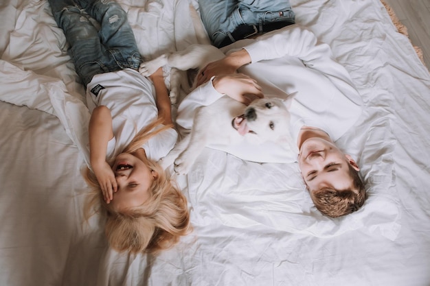 Chłopiec i dziewczynka w białych podkoszulkach, brat i siostra leżą w pościeli z białą pościelą z psem. widok z góry. ulubione zwierzę. miejsce na tekst. Zdjęcie wysokiej jakości