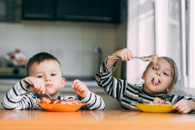 Chłopiec i dziewczynka w kuchni, jedzenie makaronu