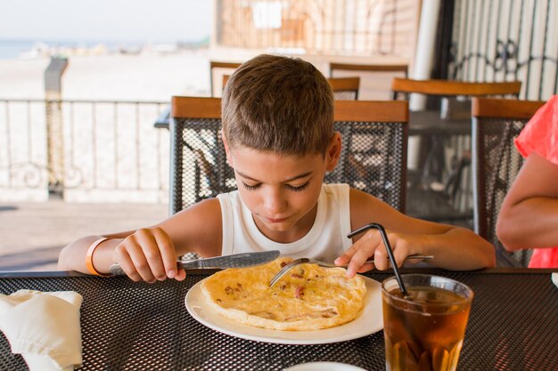 Chłopiec je omlet na piaszczystym tarasie w restauracji