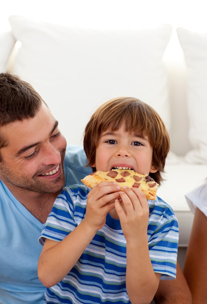 Chłopiec je pizzę w pokoju dziennym z jego ojcem