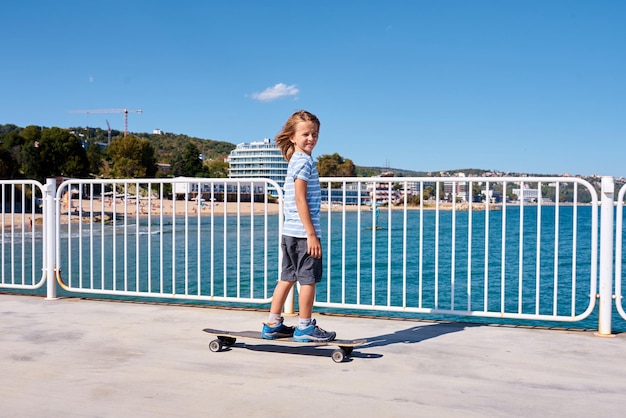 Chłopiec jedzie na longboardzie na molo w słoneczny dzień