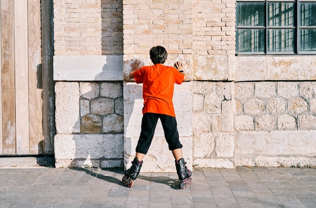 Chłopiec kaukaski od tyłu bawiący się na rolkach i przyklejony do ściany w parku.