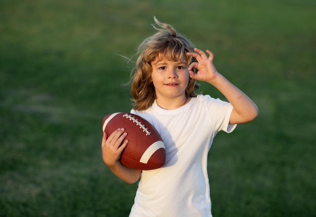 Chłopiec Kid gry z piłką do rugby w parku Chłopiec zabawy i gry w futbol amerykański na zielony gr