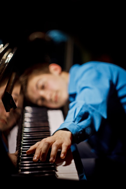 chłopiec leży na klawiszach i gra na instrumencie klawiszowym w szkole muzycznej.