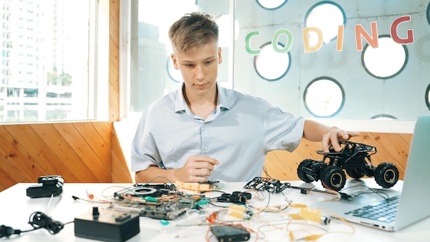 Chłopiec naprawiający model samochodu z laptopem i narzędziem elektrycznym umieszczonym na stole