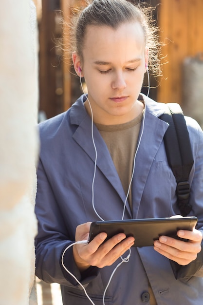 Chłopiec nastolatek wygląda na tablecie. Młody człowiek, uczeń słucha muzyka na ulicie.