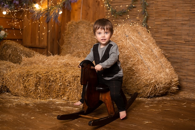 Chłopiec obsiadanie na zabawkarskim koniu w rolnym tle z słomianymi snopami