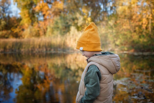 Chłopiec patrzy na piękny widok jesiennego lasu i jego odbicie w wodzie jeziora zamyślone