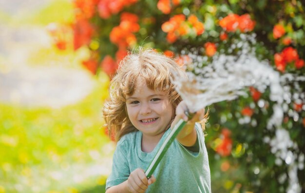 Chłopiec podlewania roślin w ogrodzie. Pojęcie dobroci dziecka i dzieciństwa. Mały pomocnik. Śliczny blond dziecko trzymając wąż do wody ogrodnictwo w domu na świeżym powietrzu w lecie.