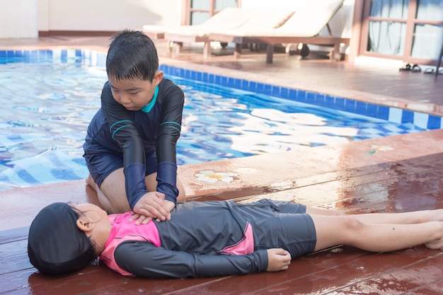 Chłopiec pomaga tonięcie dziecko dziewczyna w pływackim basenie robić CPR.