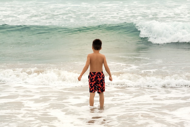 Chłopiec pozycja na plaży i patrzeć ocean fala, wakacje i podróży pojęcie ,.