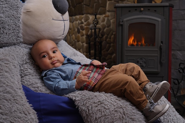 Zdjęcie chłopiec relaksuje się na dużym misiu przy kominku w domu