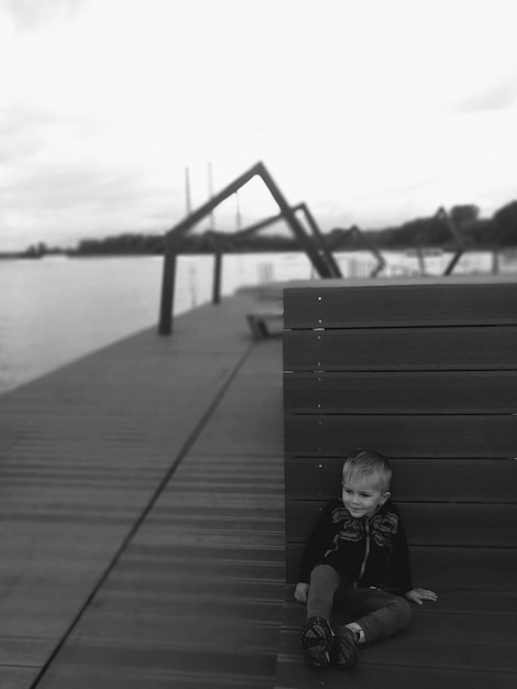 Zdjęcie chłopiec siedzący na molo nad jeziorem na tle nieba