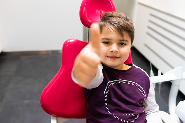 Chłopiec siedzi na krześle u dentysty i pokazuje kciuk do góry