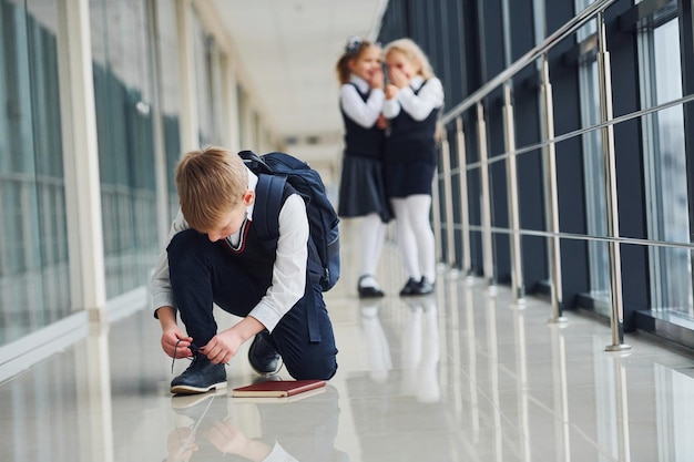 Chłopiec siedzi na podłodze Dzieci w szkole w mundurach razem na korytarzu