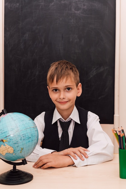 Chłopiec siedzi w szkolnej ławce na lekcji geografii