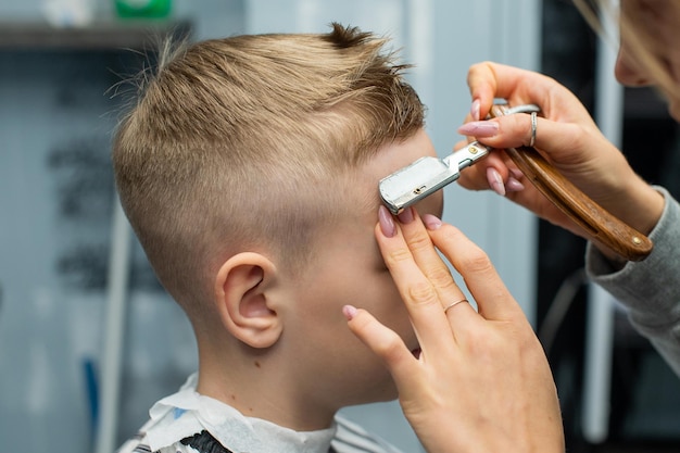 Chłopiec siedzi w zakładzie fryzjerskim i robi sobie włosy brzytwą do strzyżenia