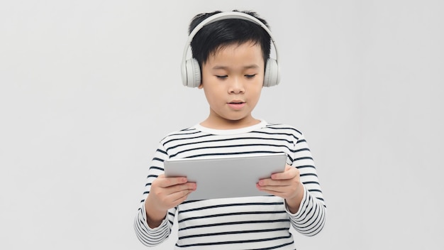Chłopiec słucha muzyki lub ogląda film w słuchawkach i gra na cyfrowym tablecie