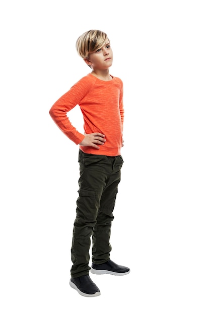 Chłopiec stoi z rękami na pasku. Facet w ciemnych dżinsach i pomarańczowym swetrze. Na białym tle. Pionowy.