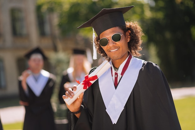 chłopiec stojący przed uniwersytetem z dyplomem w ręku