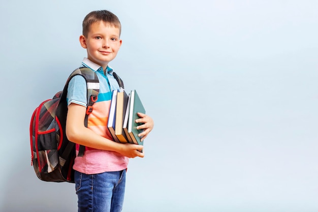 Chłopiec szkolny z plecakiem trzymający książki na niebieskim tle dla koncepcji edukacji