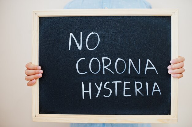 Chłopiec trzyma na tablicy napis z tekstem No corona histeria
