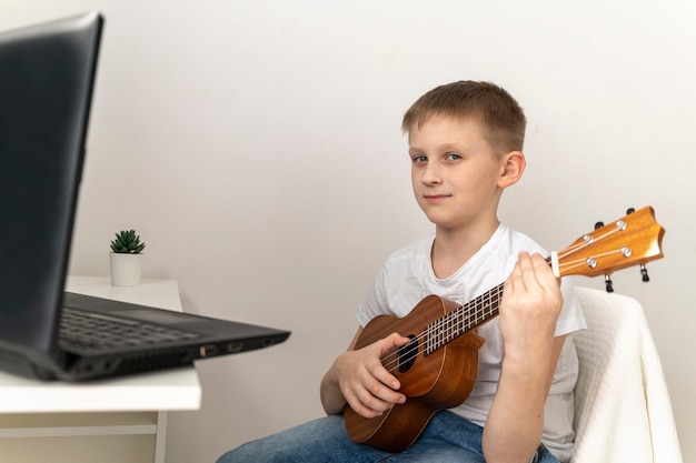 Chłopiec uczy się grać na ukulele na laptopie.