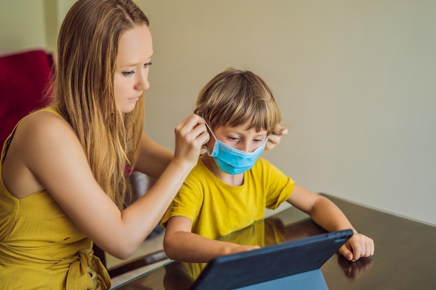 Chłopiec uczy się online w domu za pomocą tabletu Mama pomaga mu się uczyć Mama i syn w maskach medycznych w celu ochrony przed koronowirusem Nauka podczas kwarantanny Globalny wirus pandemiczny covid19