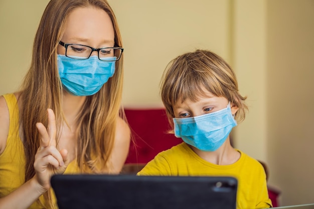 Chłopiec uczy się online w domu za pomocą tabletu Mama pomaga mu się uczyć Mama i syn w maskach medycznych w celu ochrony przed koronowirusem Nauka podczas kwarantanny Globalny wirus pandemiczny covid19