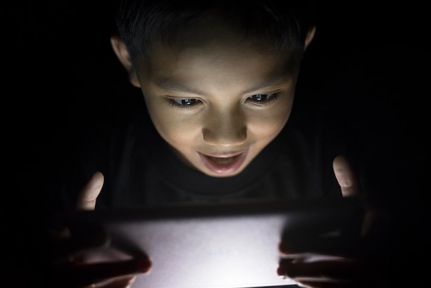 Zdjęcie chłopiec używający cyfrowego tabletu w ciemni