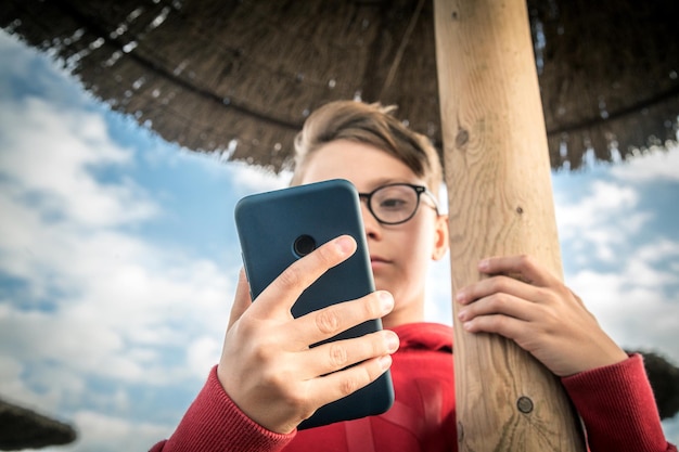 Zdjęcie chłopiec używający telefonu komórkowego pod dachem ze słomy