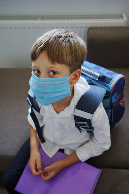 Chłopiec w masce medycznej z plecakiem czekający na rozpoczęcie lekcji