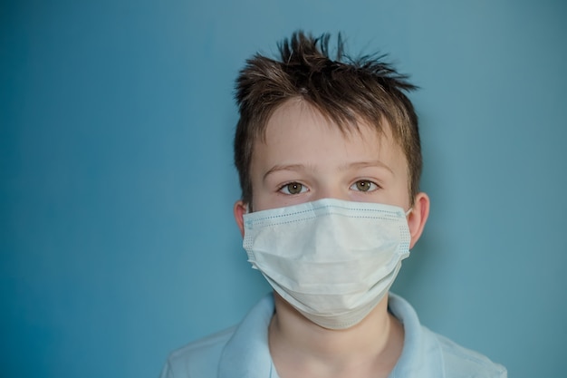 Chłopiec w medycznej masce na błękit ścianie. dziecko z grypą wśród pacjentów z koronawirusem