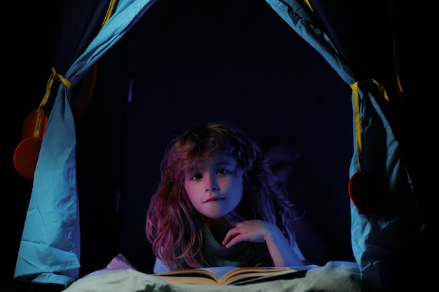 Zdjęcie chłopiec w namiocie dla dzieci czyta książki w kierunku wiedzy chłopiec z książką czyta historię ciesz się nauką i czytaniem