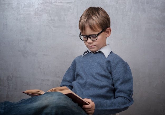 Chłopiec W Okularach, Czytając Książkę, Siedząc Na Krześle W Pokoju
