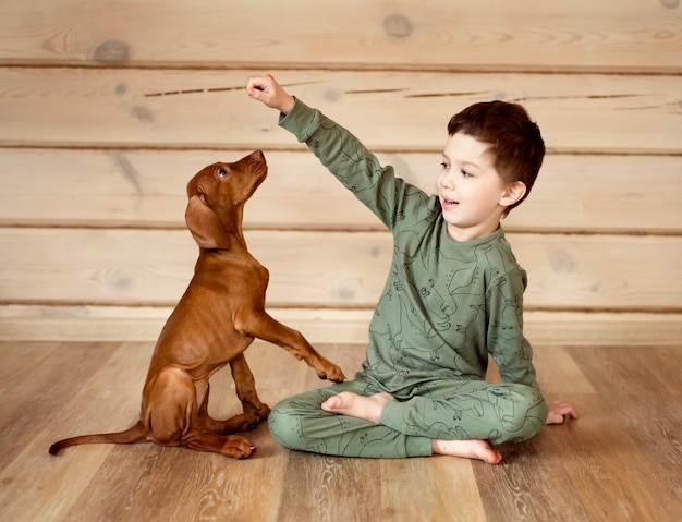 Chłopiec w piżamie bawi się ze szczeniakiem w drewnianym domu